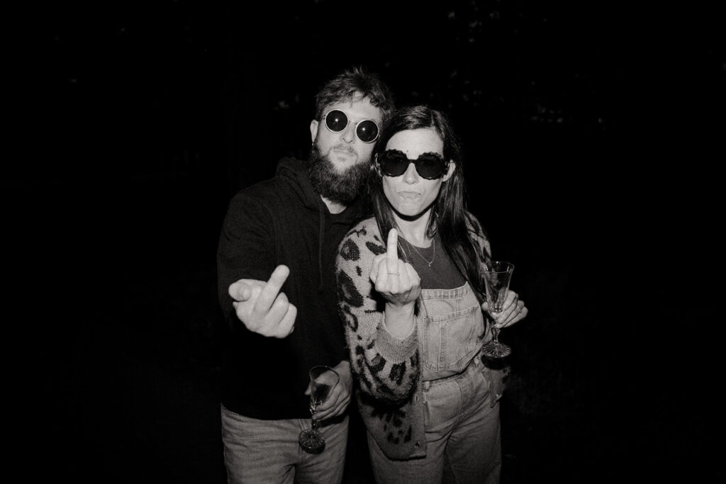 Caroline et fabien de nuit buvant une coupe de champagne et faisant un doigt d'honneur à la caméra. Photo en noir et blanc.