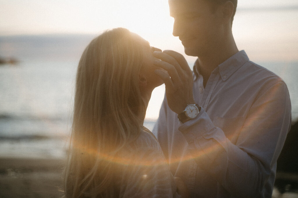 Couple les yeux dans les yeux à contre jour dans une décor de plage pour une séance photo d'engagement.